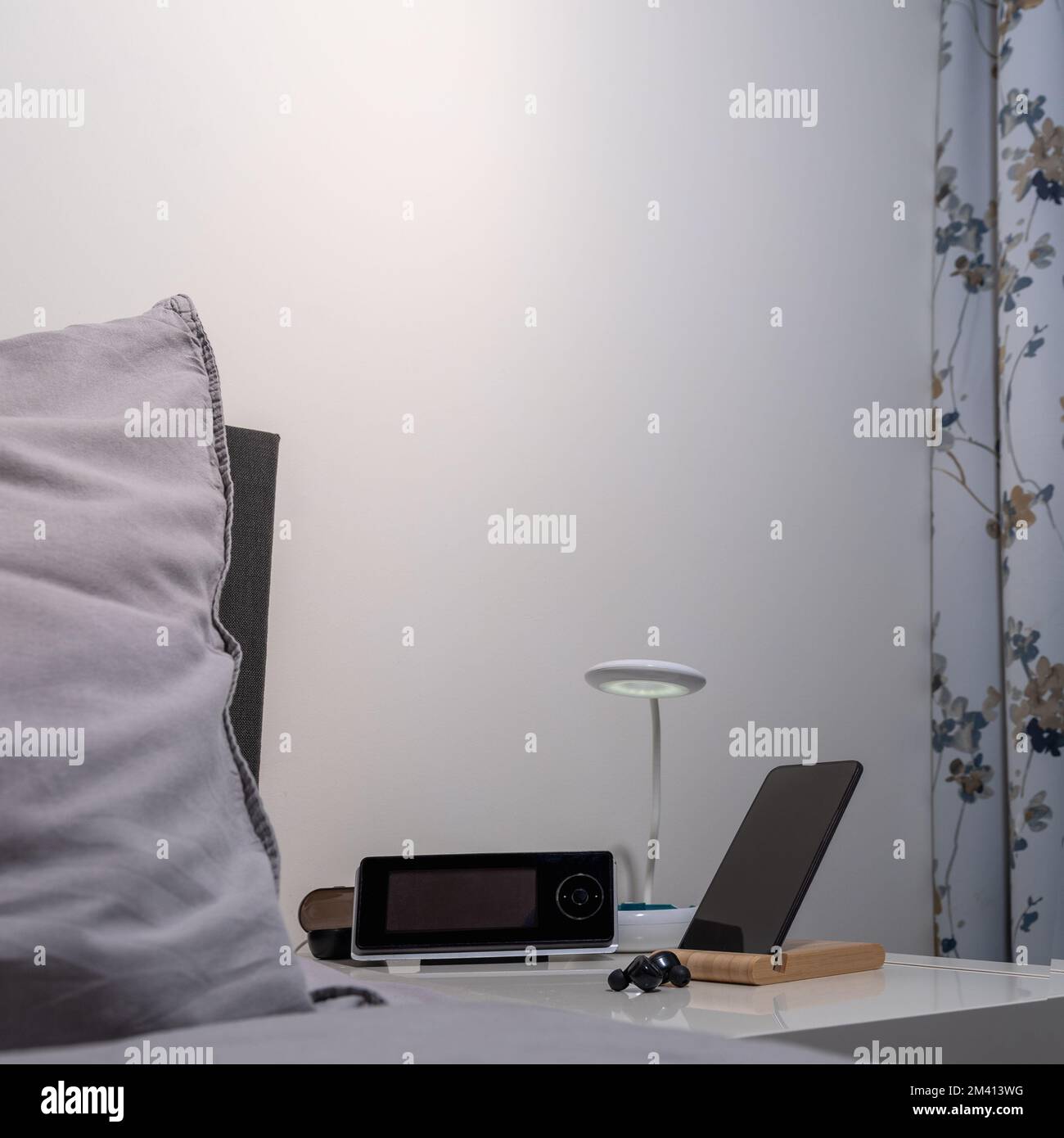 Nachttisch mit Lampe, Smartphone, Headset und Cloc. Quadratisches Format Stockfoto