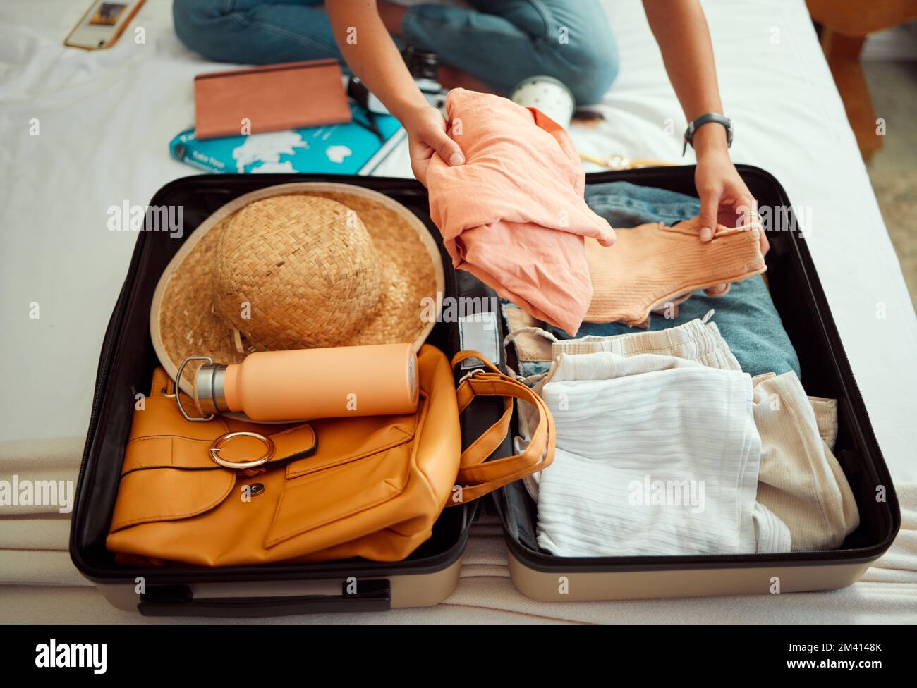 Hände, Frau und Koffer auf einem Bett für Reisen, Abenteuer und Sommerurlaub, Packungen und Kleidung. Hand, Mädchen und Gepäck in einem Schlafzimmer zum Reisen Stockfoto