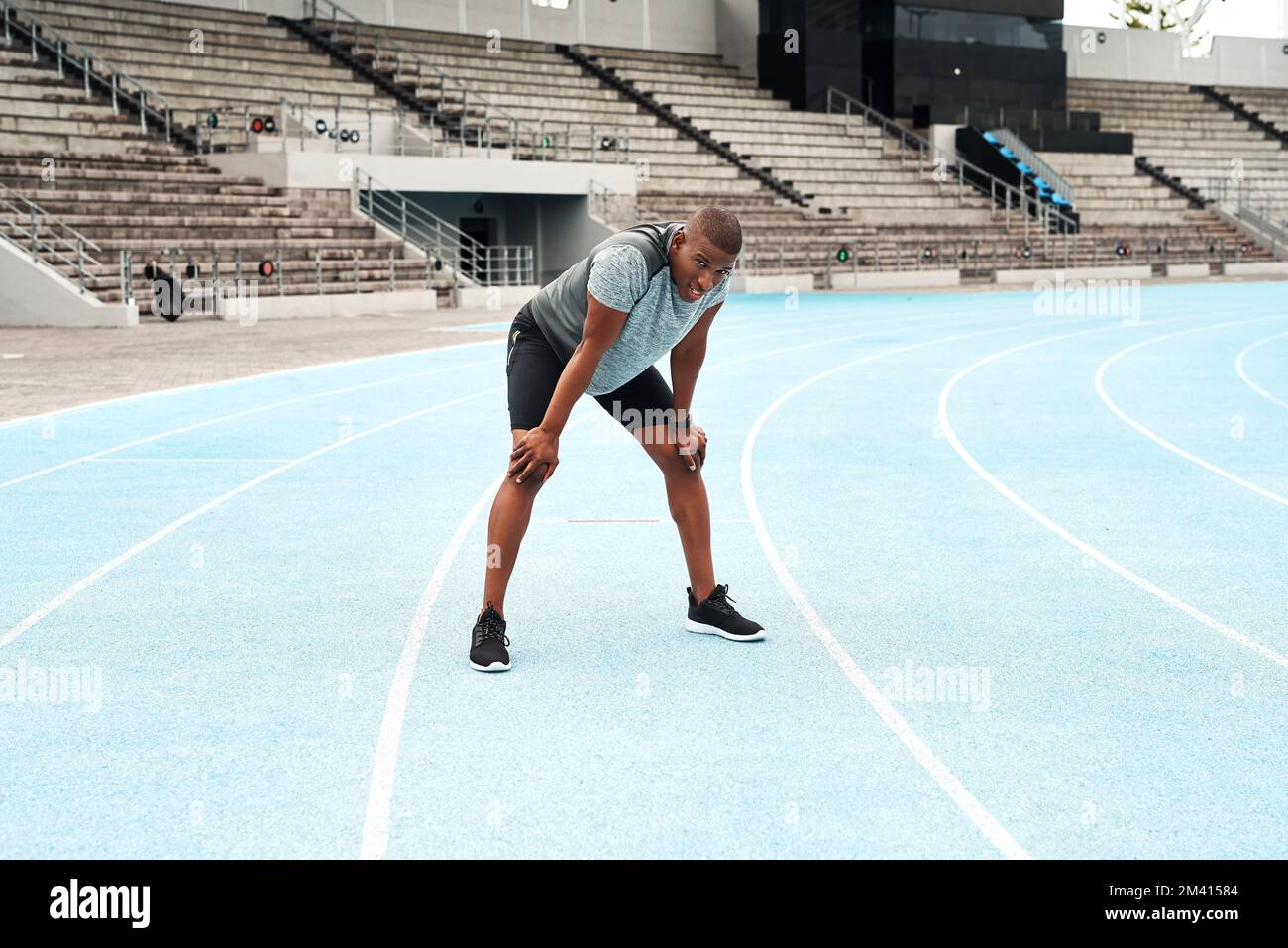 Puh, das hat sich gut angefühlt. Ein langes Porträt eines gutaussehenden jungen Athleten, der allein auf einem Leichtathletikfeld steht und nach dem Laufen Luft schnappt. Stockfoto