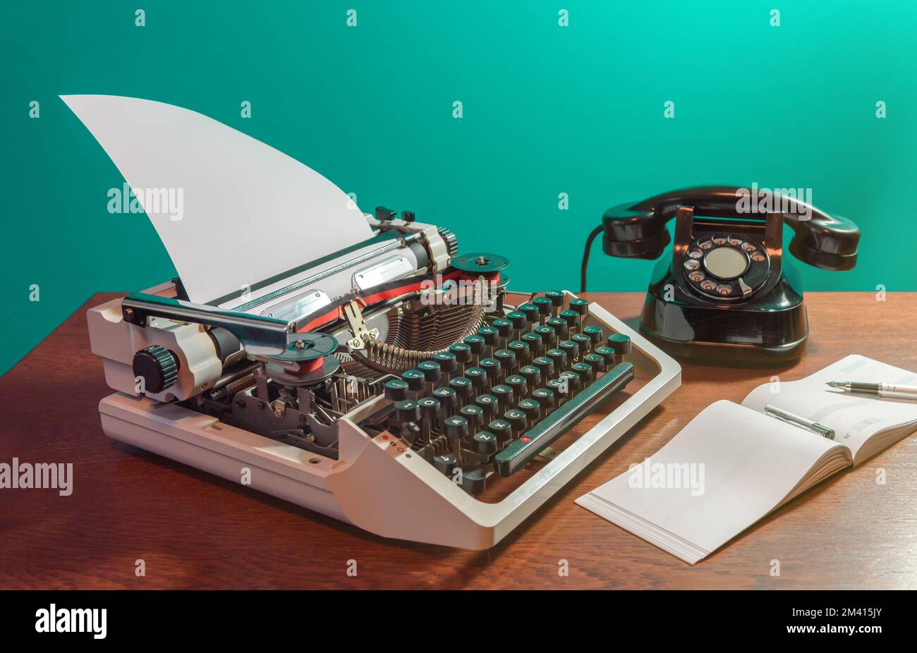 Eine Retro-Schreibmaschine und ein altes Telefon liegen auf dem Tisch, zusammen mit einem Scheckbuch und einem Tintenstift. Stockfoto