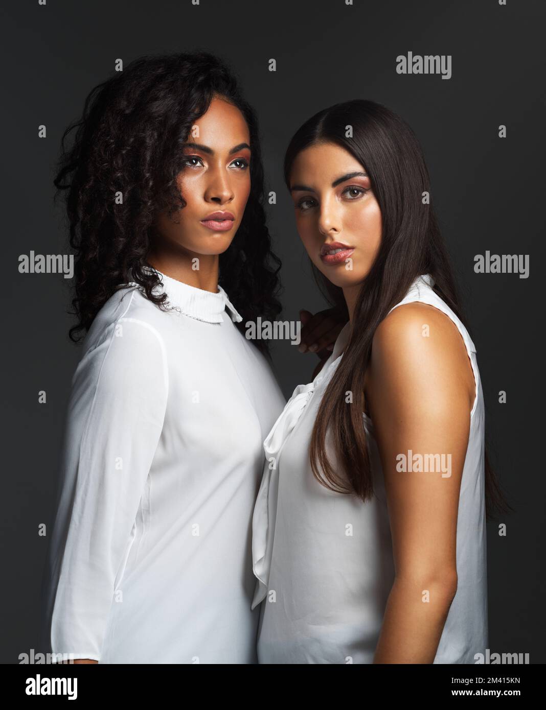 Frauen sind die wahren Architekten der Welt. Studiofoto von zwei attraktiven jungen Frauen, die weiße Blusen tragen und sich eng gegen eine Dunkelheit aufstellen Stockfoto