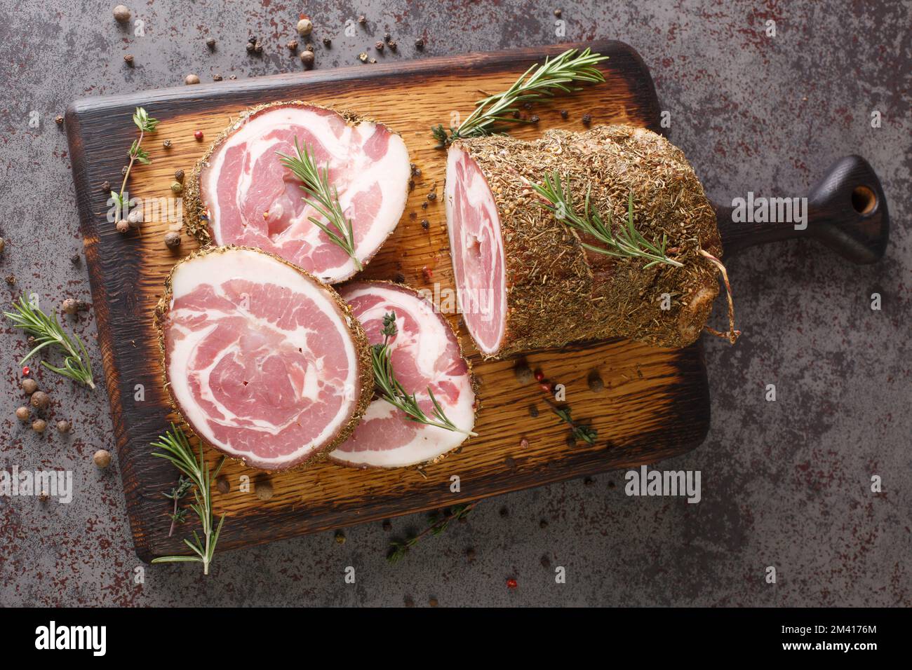 Pancetta ist geräucherter Schweinebauch, der mit Salz, Kräutern und Gewürzen auf dem Holzbrett auf dem Tisch hergestellt wird. Horizontale Draufsicht von oben Stockfoto