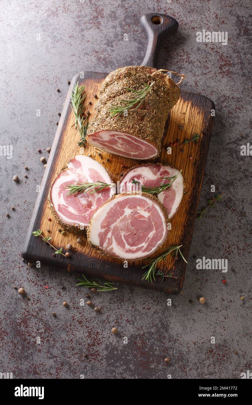 Pancetta ist eine salzgepökelte Schweinefleisch-Bauchfleischrolle auf dem Holzbrett auf dem Tisch. Vertikale Draufsicht von oben Stockfoto