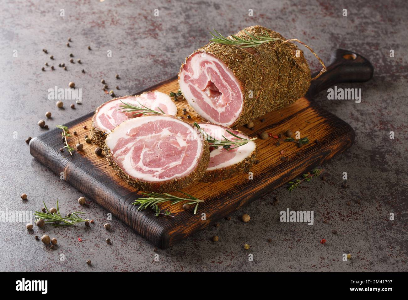 Pancetta ist geräucherter Schweinebauch, der mit Salz, Kräutern und Gewürzen auf dem Holzbrett auf dem Tisch hergestellt wird. Horizontal Stockfoto