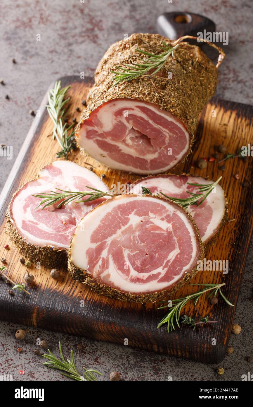 Pancetta ist eine salzgepökelte Schweinefleisch-Bauchfleischrolle auf dem Holzbrett auf dem Tisch. Vertikal Stockfoto