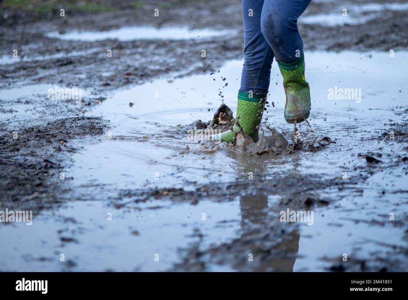 Nahaufnahme eines Jungen in Gummistiefeln, der in Schlamm und Teich springt. Wassertropfen und Schlamm, schmutzige Hosen und Stiefel. Wasserdichtes Gummi Stockfoto