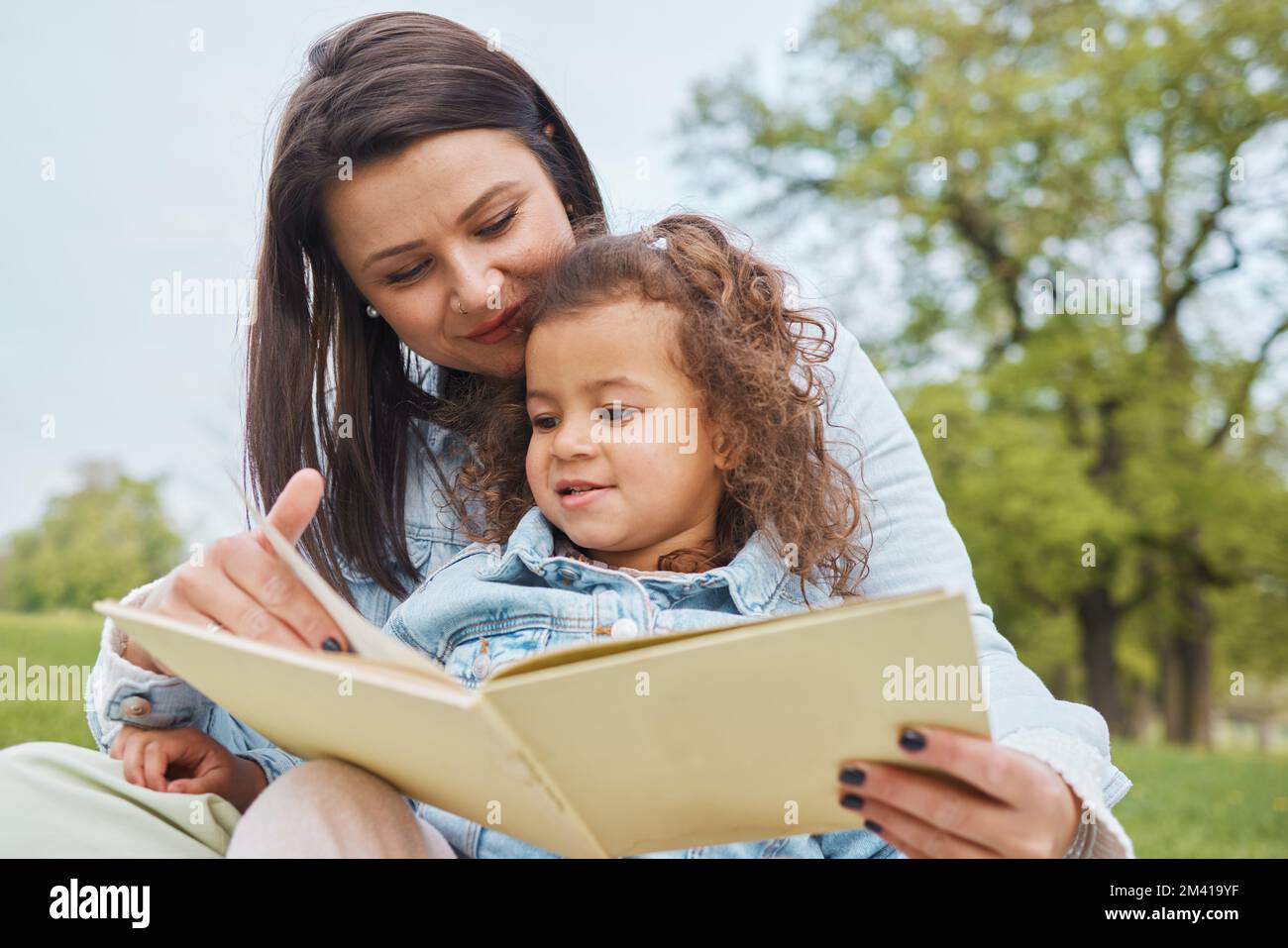 Mutter, Mädchen Buch und im Park lesen, um Geschichten zu erzählen, sich weiterzuentwickeln und sich zu entspannen, um eine Beziehung zu knüpfen. Mutter, weibliches Kind und mit Geschichten lernen Stockfoto