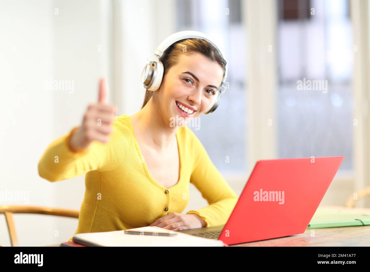 Glückliche Schülerin mit Kopfhörern und Laptop zu Hause, mit Daumen nach oben, wenn sie Sie ansieht Stockfoto