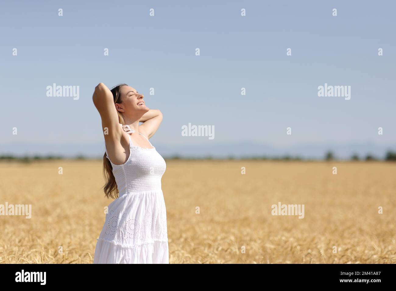 Glückliche Frau in weißem Kleid, atmet in einem goldenen Weizenfeld Stockfoto