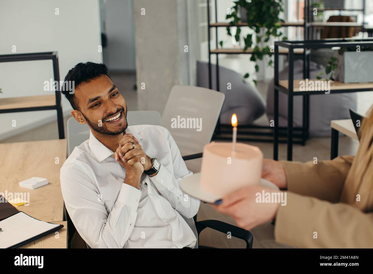 Ein junger Hindu-Mann ist dabei, Kerzen auf einem Kuchen auszublasen und sich während einer Geburtstagsfeier mit Kollegen etwas zu wünschen. Kollegen feiern eine Geburt Stockfoto