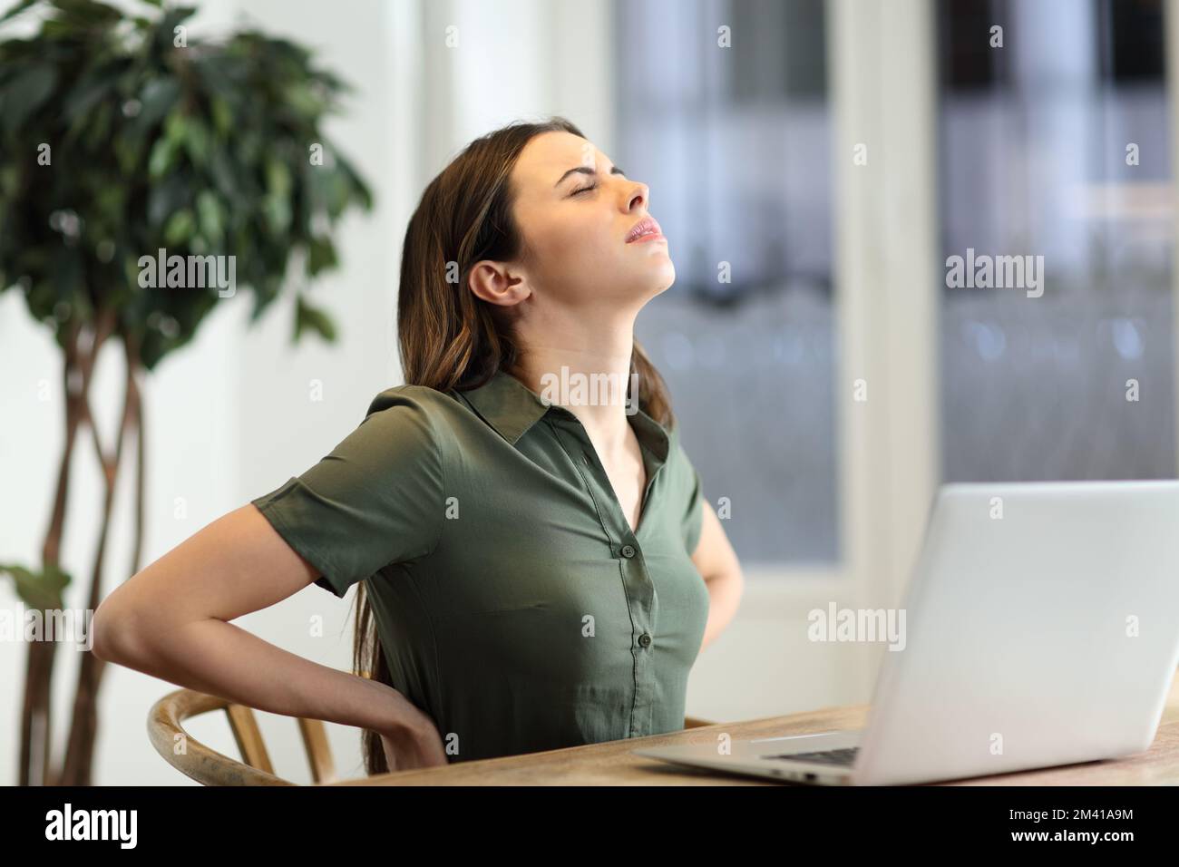 Frau mit einem Laptop, die Rückenschmerzen hat, sitzt in einem unbequemen Stuhl Stockfoto