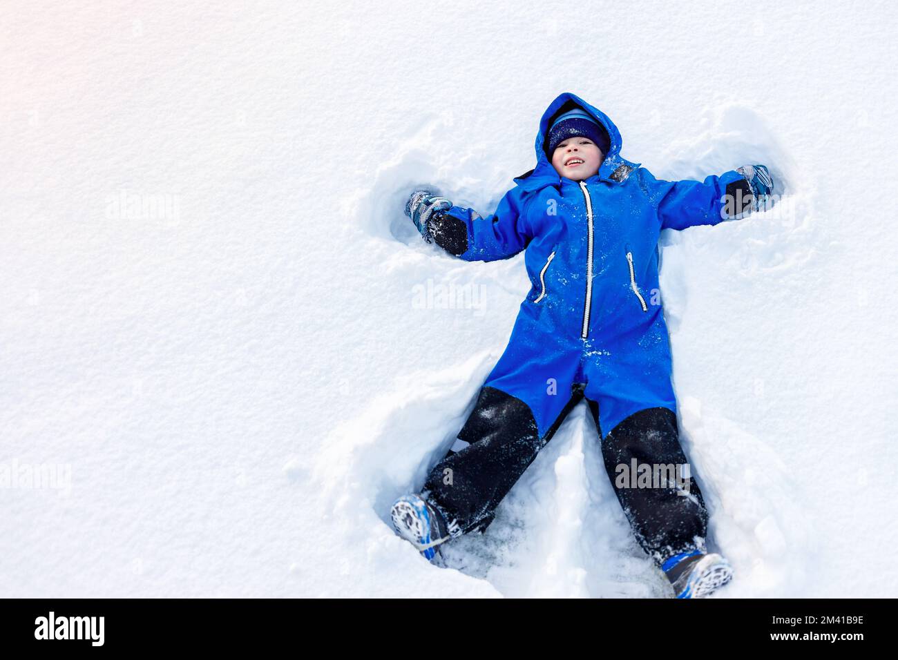 Ein glücklicher kleiner Junge macht einen Schneeengel Stockfoto