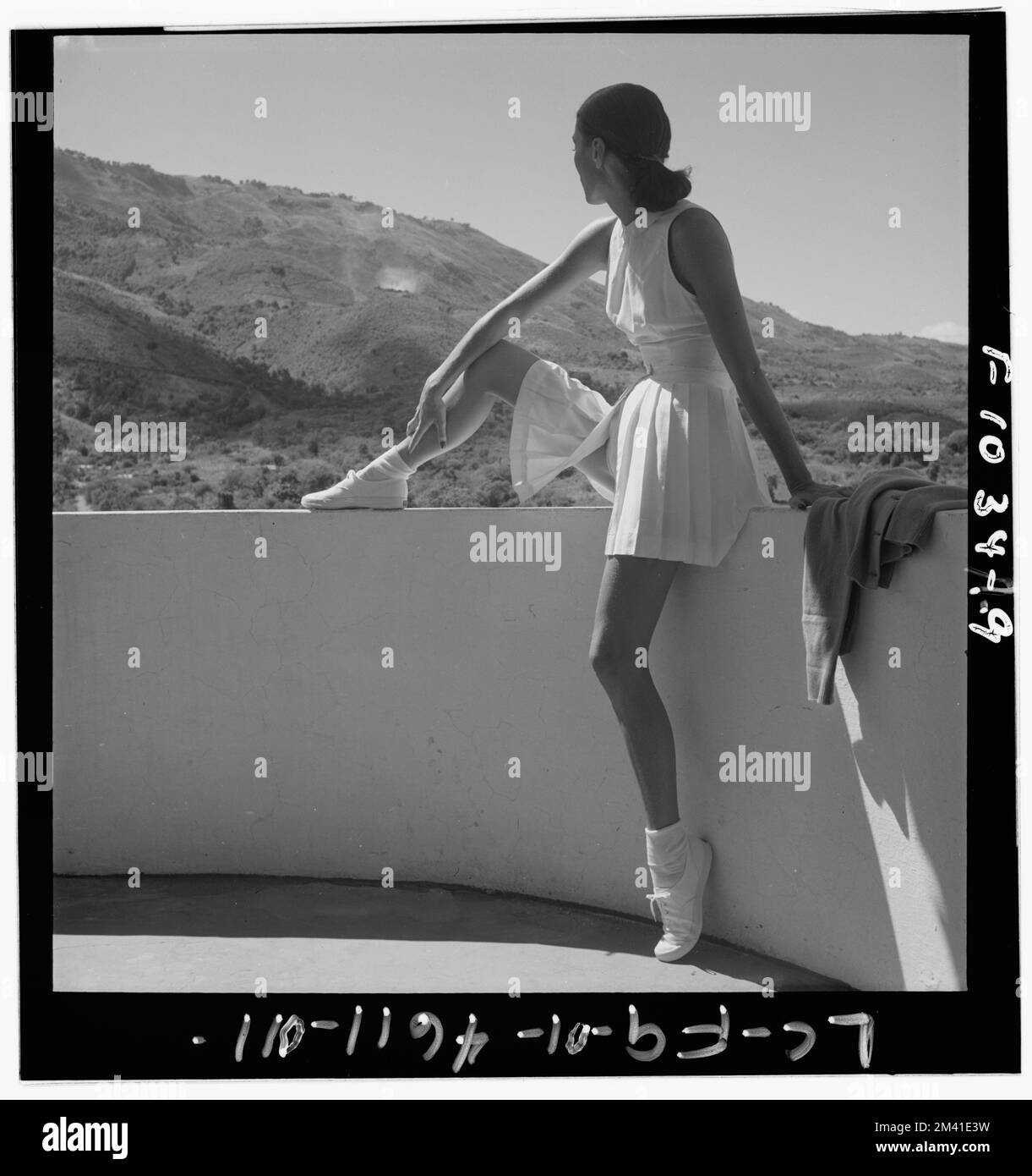 Modemodell, das Tennis-Outfit trägt, an der Wand sitzt, mit einem Bein oben an der Wand, mit Blick auf die Berge hinter ihr, Toni Frissell, Antoinette Frissell Bacon, Antoinette Frissell Stockfoto