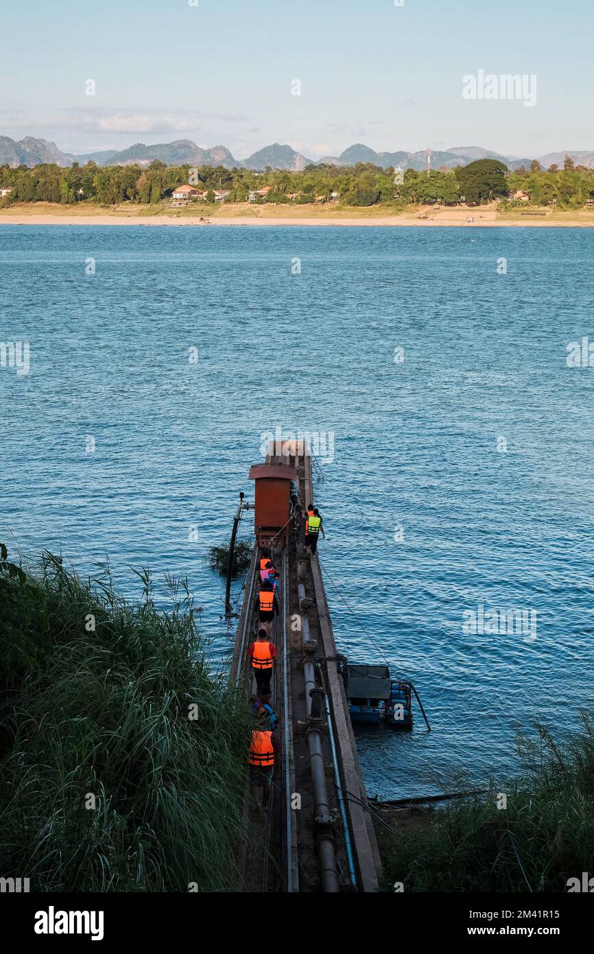 Eine Gruppe von Personen mit Schwimmwesten, die entlang des Mekong mit wunderschönen Laos-Bergen im Hintergrund spazieren Stockfoto