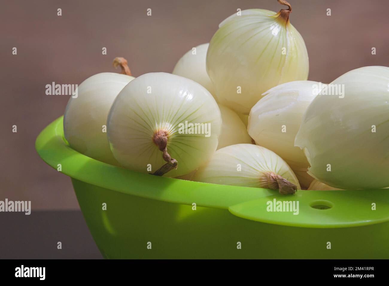 Geschälte Zwiebeln in einem grünen Kunststoffsieb. Speicherplatz kopieren. Brauner Hintergrund Stockfoto
