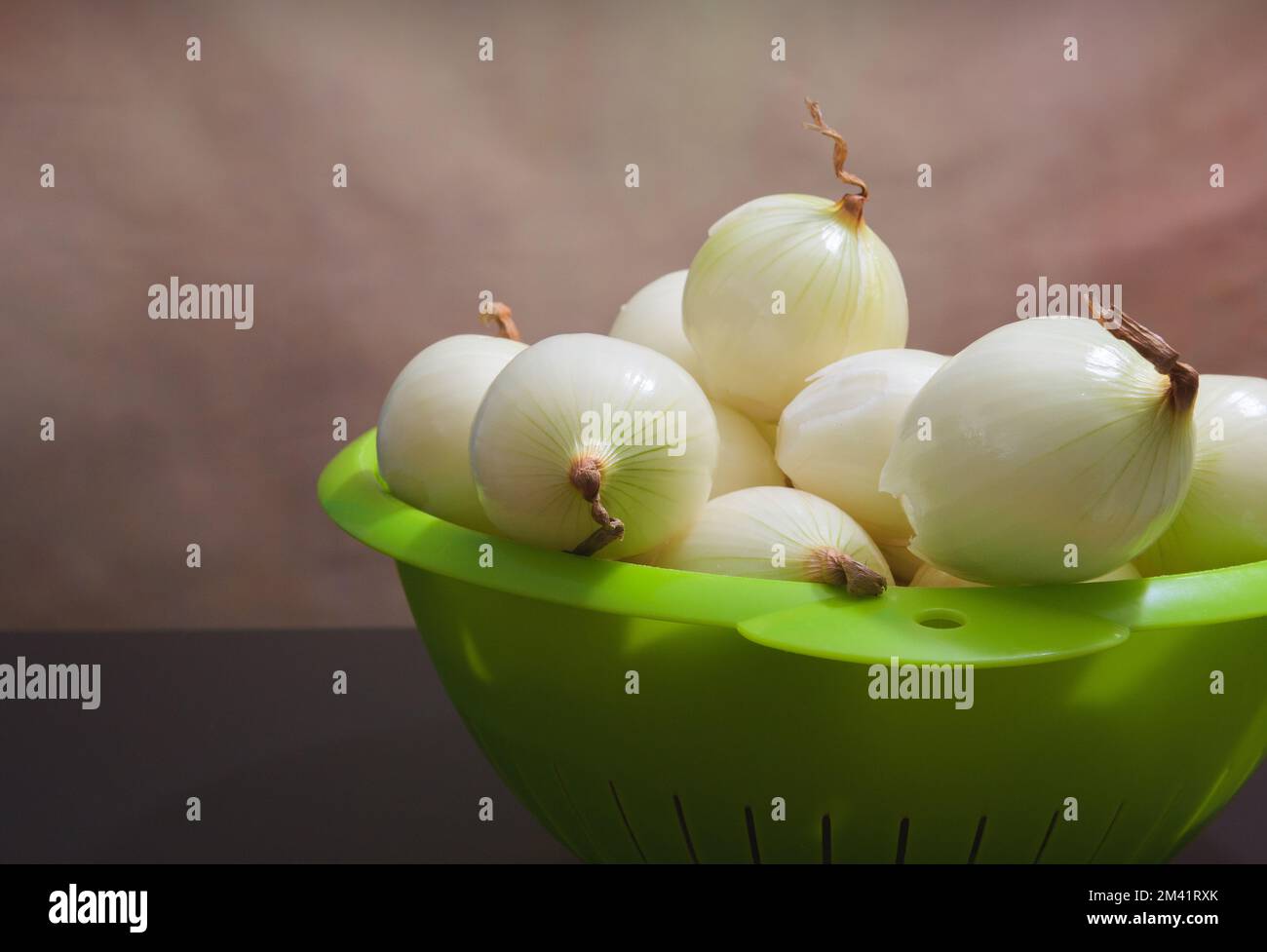 Geschälte Zwiebeln in einem grünen Kunststoffsieb. Speicherplatz kopieren Stockfoto