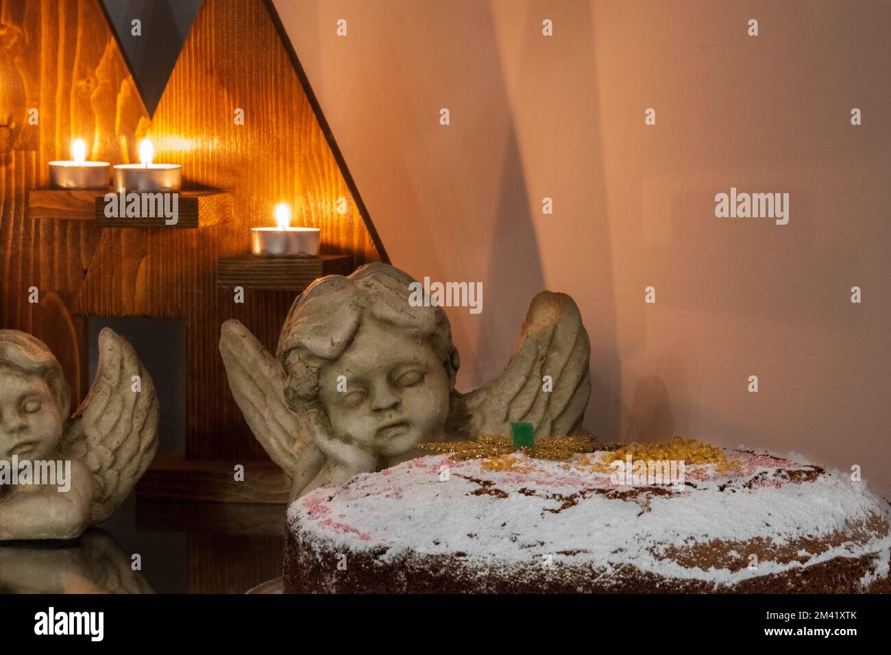 Festliches Weihnachtsgeschenk bestehend aus Kerzen, Engelsstatuen und einem Kuchen auf einem Tisch. Stockfoto