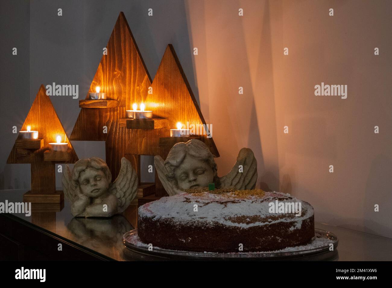 Festliches Weihnachtsgeschenk bestehend aus Kerzen, Engelsstatuen und einem Kuchen auf einem Tisch. Stockfoto