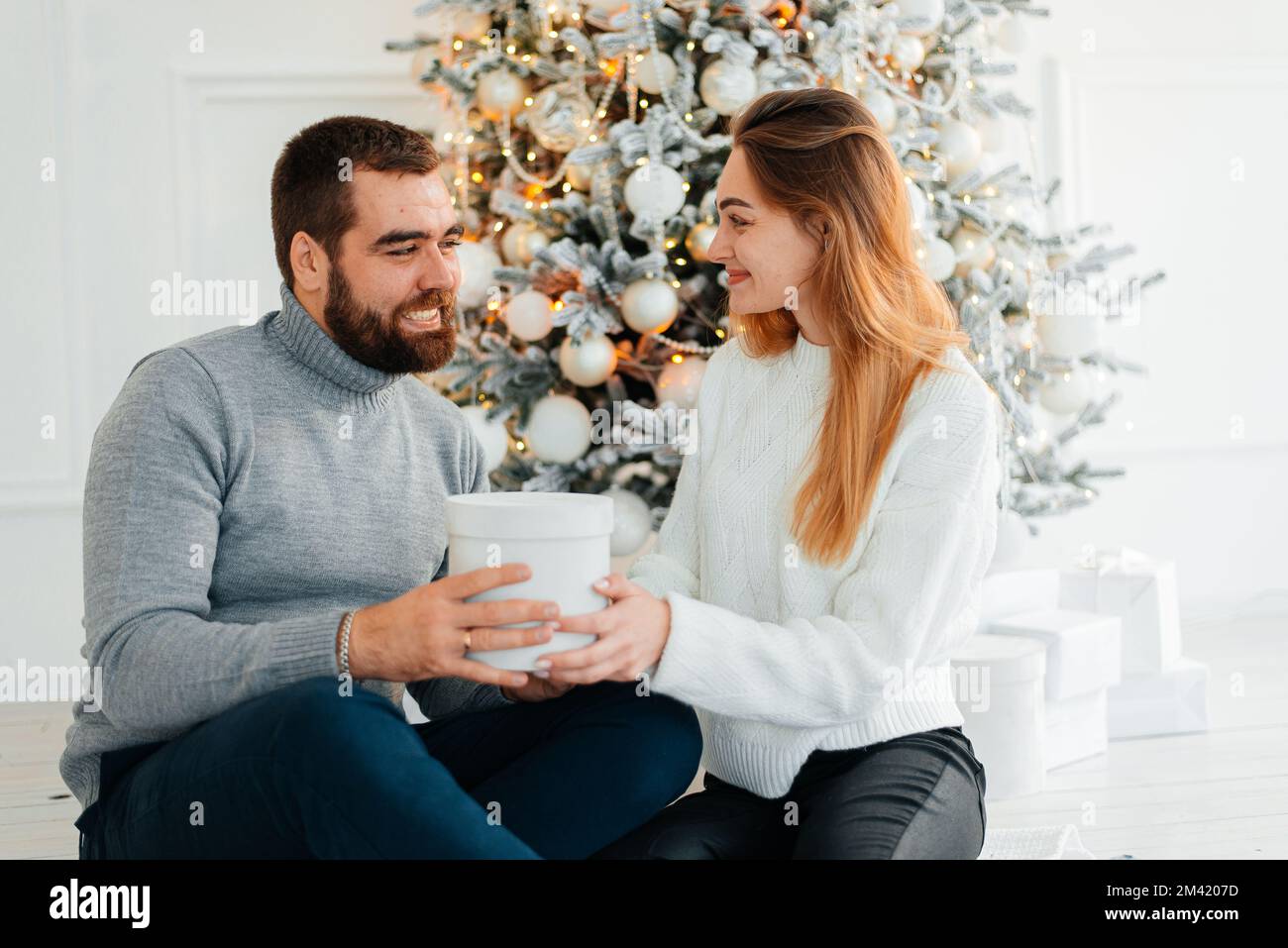 Glückliches Paar in der Nähe von Geschenkschachteln und weihnachtsbaum. Ein Paar umarmt sich und schaut sich an, nahe dem weihnachtsbaum. Stockfoto
