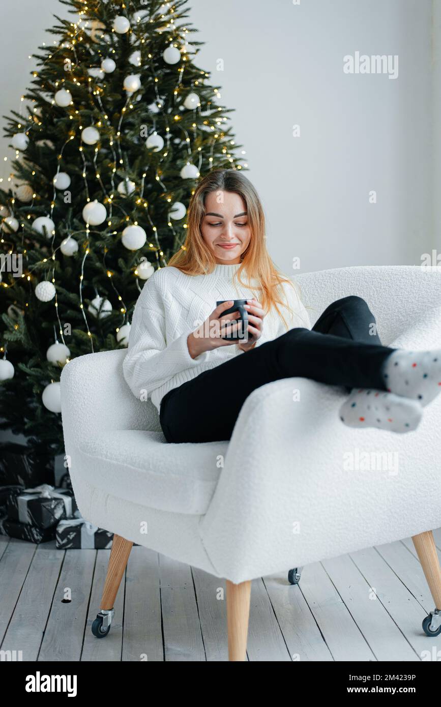 Lächelnde junge Frau Genießen Sie den Neujahrsurlaub zu Hause, träumen Sie oder stellen Sie sich eine fröhliche Zukunft vor. Stockfoto