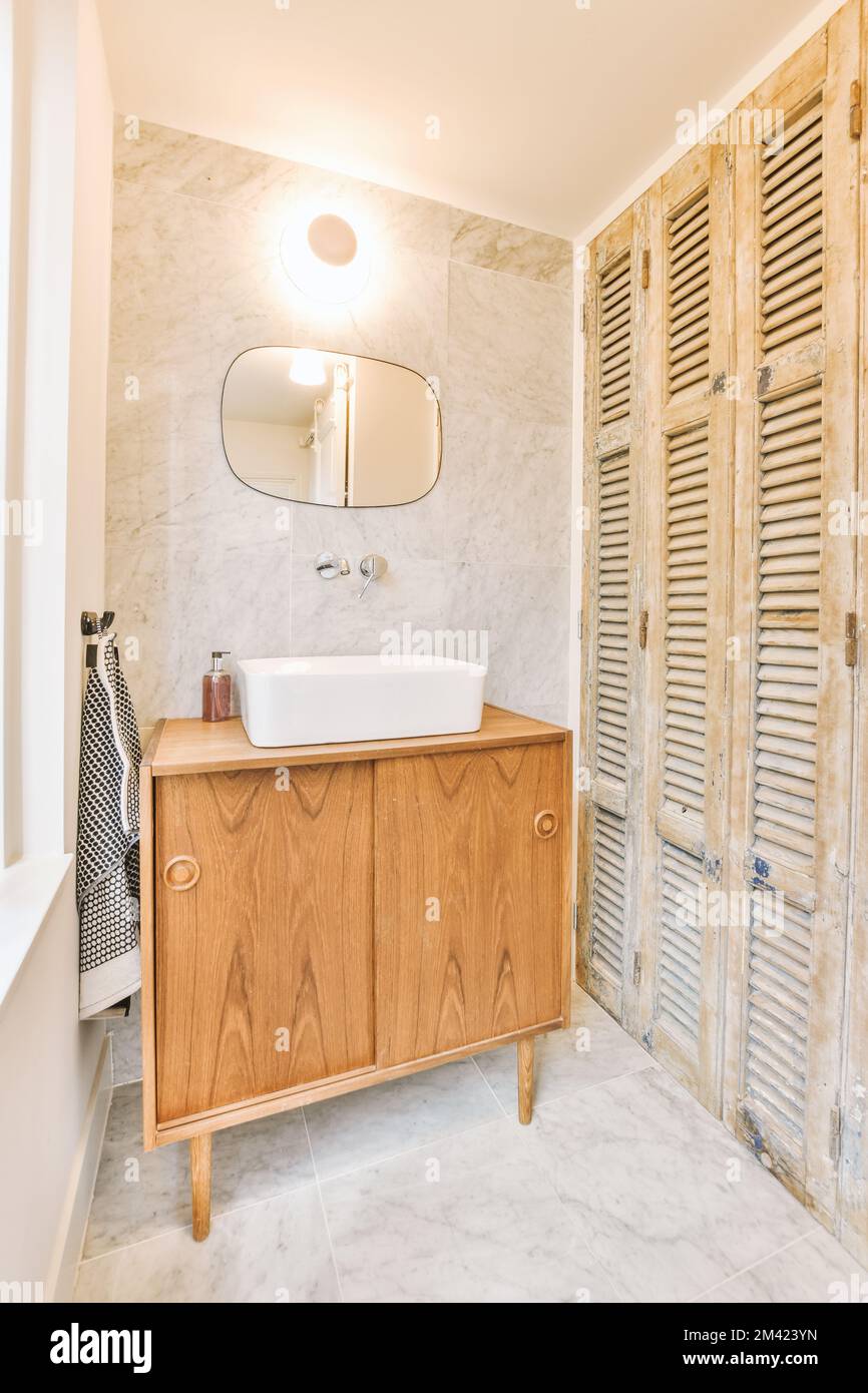 Neben dem Waschbecken befindet sich ein Badezimmer mit Holzläden an der Wand und weißem Marmorboden in der Duschkabine Stockfoto