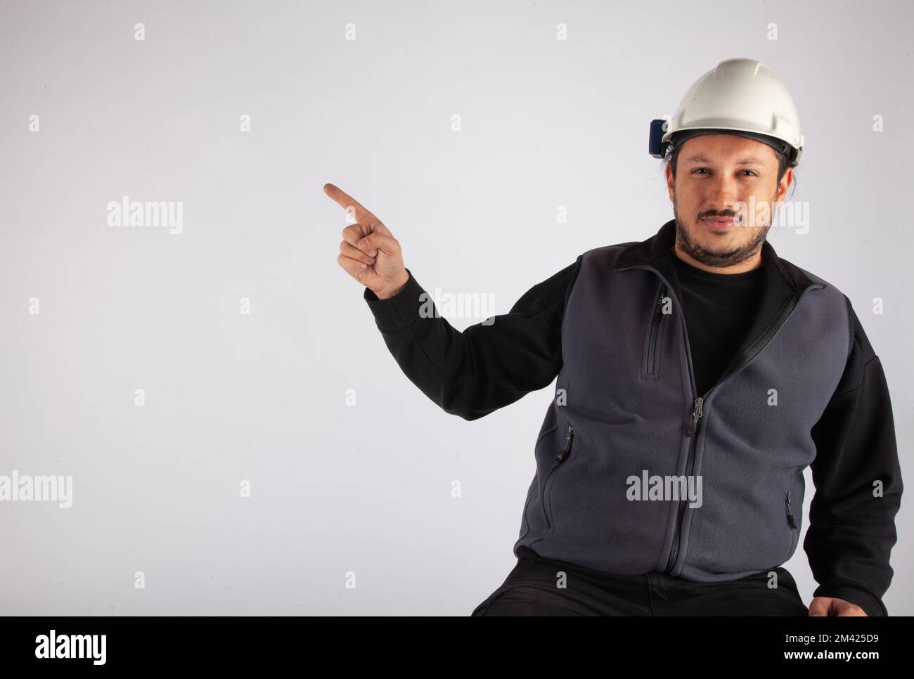 Mann mit weißem Schutzhelm, der auf einen leeren Textbereich auf isolierten weißen Hintergrund zeigt. Stockfoto