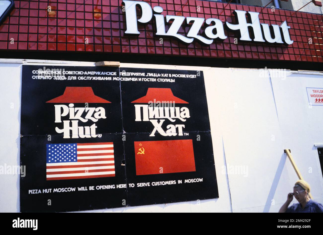 Schild vor dem „Development of the First Pizza Hut Restaurant“, das in Moskau nach einer Veränderung in der Sowjetunion während der Perestroika eröffnet wird. Schilder, die die Eröffnung in amerikanischer und russischer Sprache mit der russischen Flagge und der amerikanischen Flagge anpreisen, aufgenommen 1990 Stockfoto