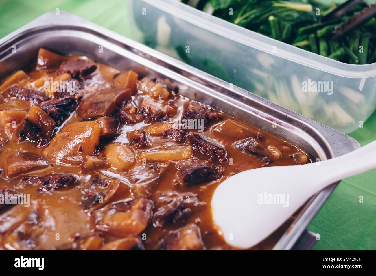 Köstlicher philippinischer Oxtail und dreifaches Eintopf in reichhaltiger und dicker Erdnusssoße oder „Kare Kare“ in einer Servierschale aus Edelstahl neben dem grünen Gemüse Stockfoto