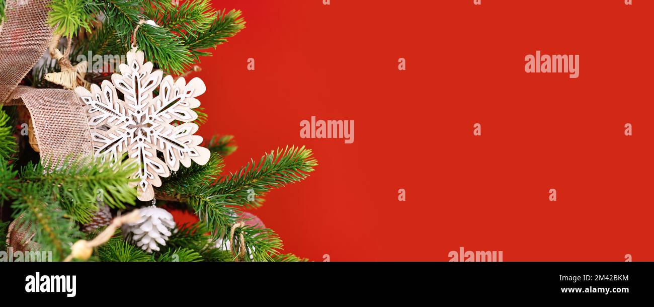 Weihnachtsbanner mit Baumzweig mit natürlicher Holzschneeflocke vor rotem Hintergrund mit Kopierbereich Stockfoto
