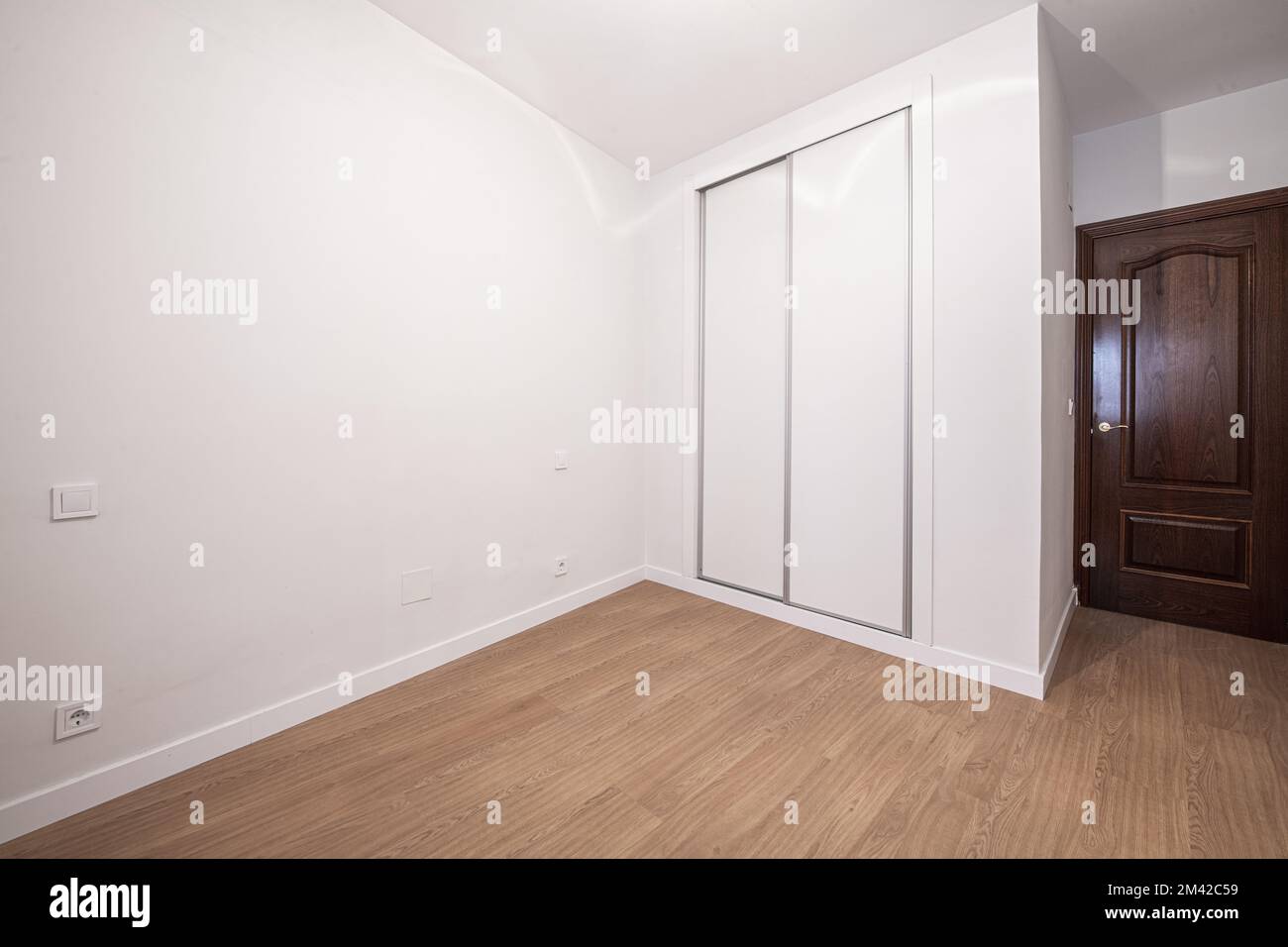 Ein Zimmer mit einem speziell angefertigten Kleiderschrank mit weißen Schiebetüren, weiß bemalten glatten Wänden und dunklen Holztüren Stockfoto