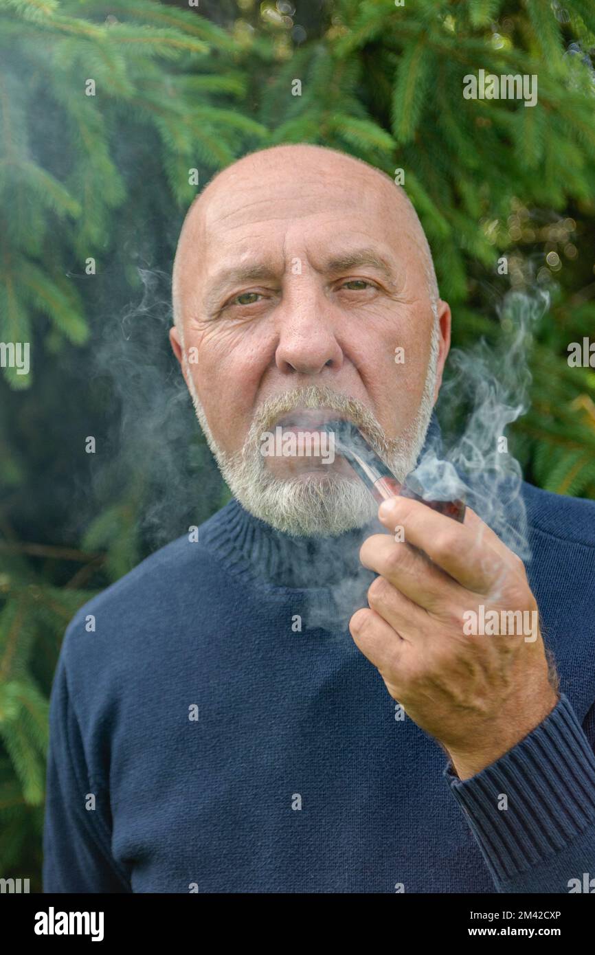 Ein älterer Mann mit grauem Bart und einer Raucherpfeife im Wald Stockfoto