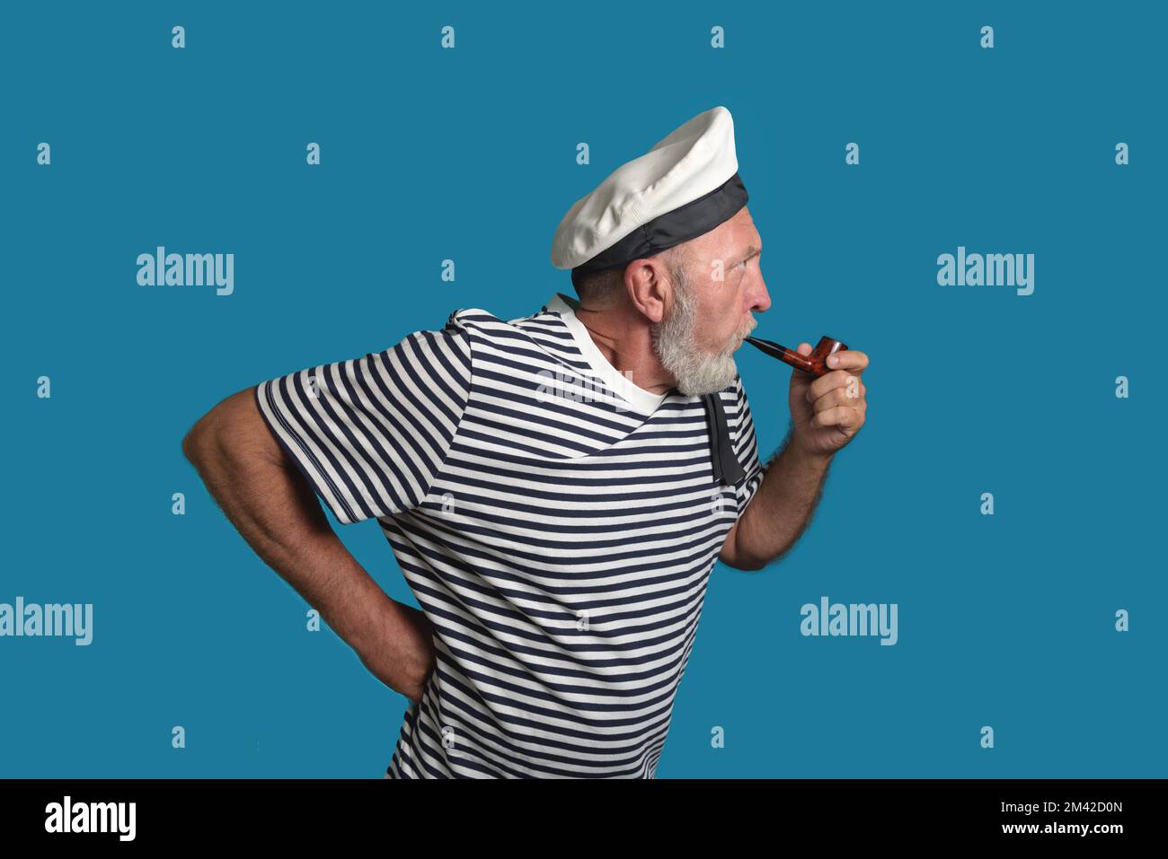 Aufmerksamer Seemann. Ein alter Seemann mit einer Rauchpfeife auf blauem Hintergrund isoliert Stockfoto