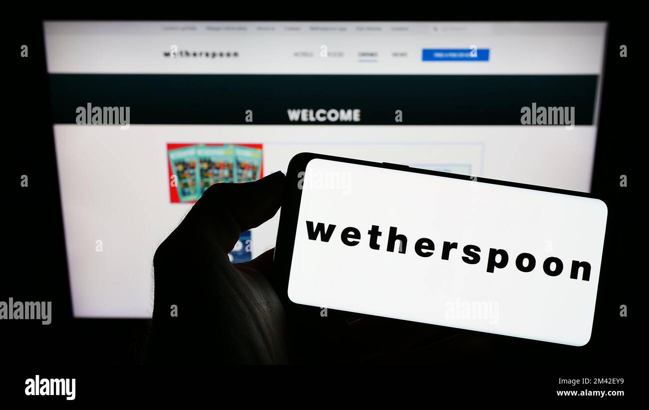 Person, die ein Smartphone mit dem Logo des britischen Pub-Unternehmens J D Wetherspoon plc auf dem Bildschirm vor der Website hält. Konzentrieren Sie sich auf das Display des Telefons. Stockfoto