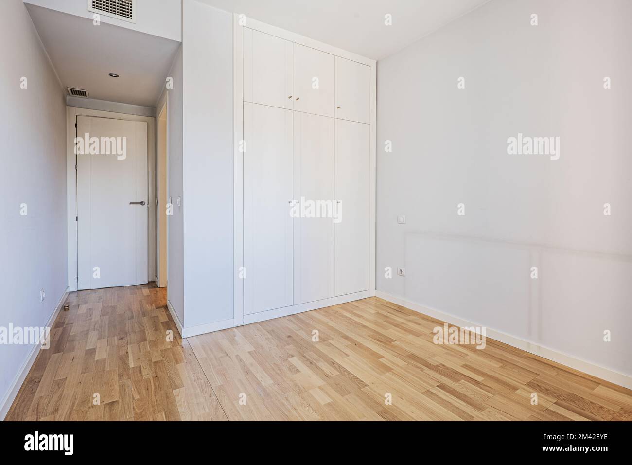 Leerer Raum mit eingebautem Kleiderschrank mit weißen Holztüren mit passenden Kofferräumen und Klimakanälen in der abgehängten Decke Stockfoto