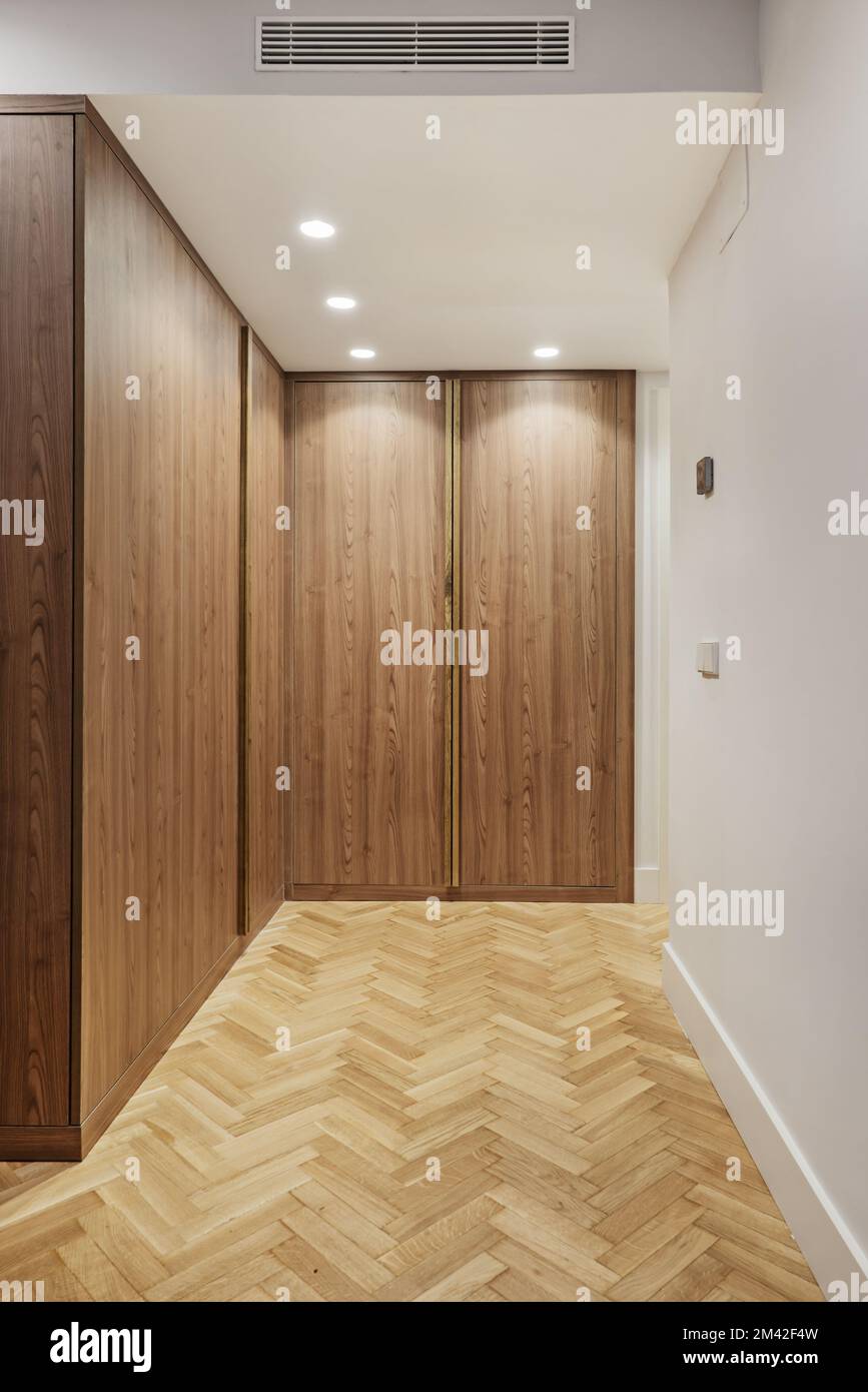 Holzgarderobe mit glatten Türen in einem Raum mit Eichenboden mit Fischgrätenmuster, Spots in der Zwischendecke und Klimaanlage Stockfoto