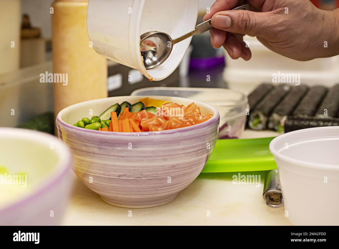 Ein Koch, der in einer asiatischen Küche eine Lachs-Schüssel mit Mohnsamen zubereitet Stockfoto