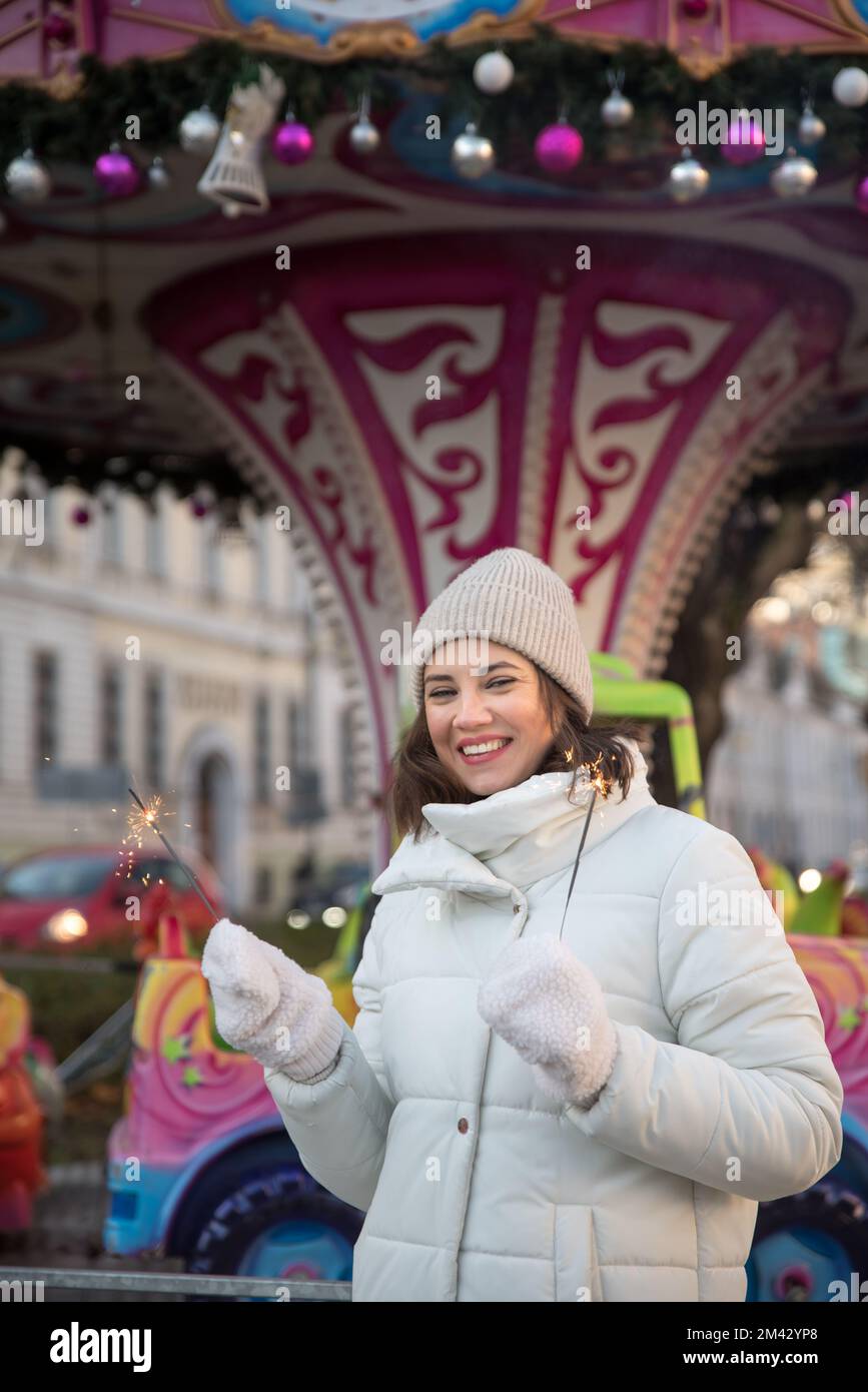 Das ist fair. Attraktionen, Karussell . Ein Mädchen in einer weißen Jacke und einem weißen Hut. Das Mädchen lächelt. Das Mädchen freut sich. Emotionen. Wir feiern Weihnachten Stockfoto