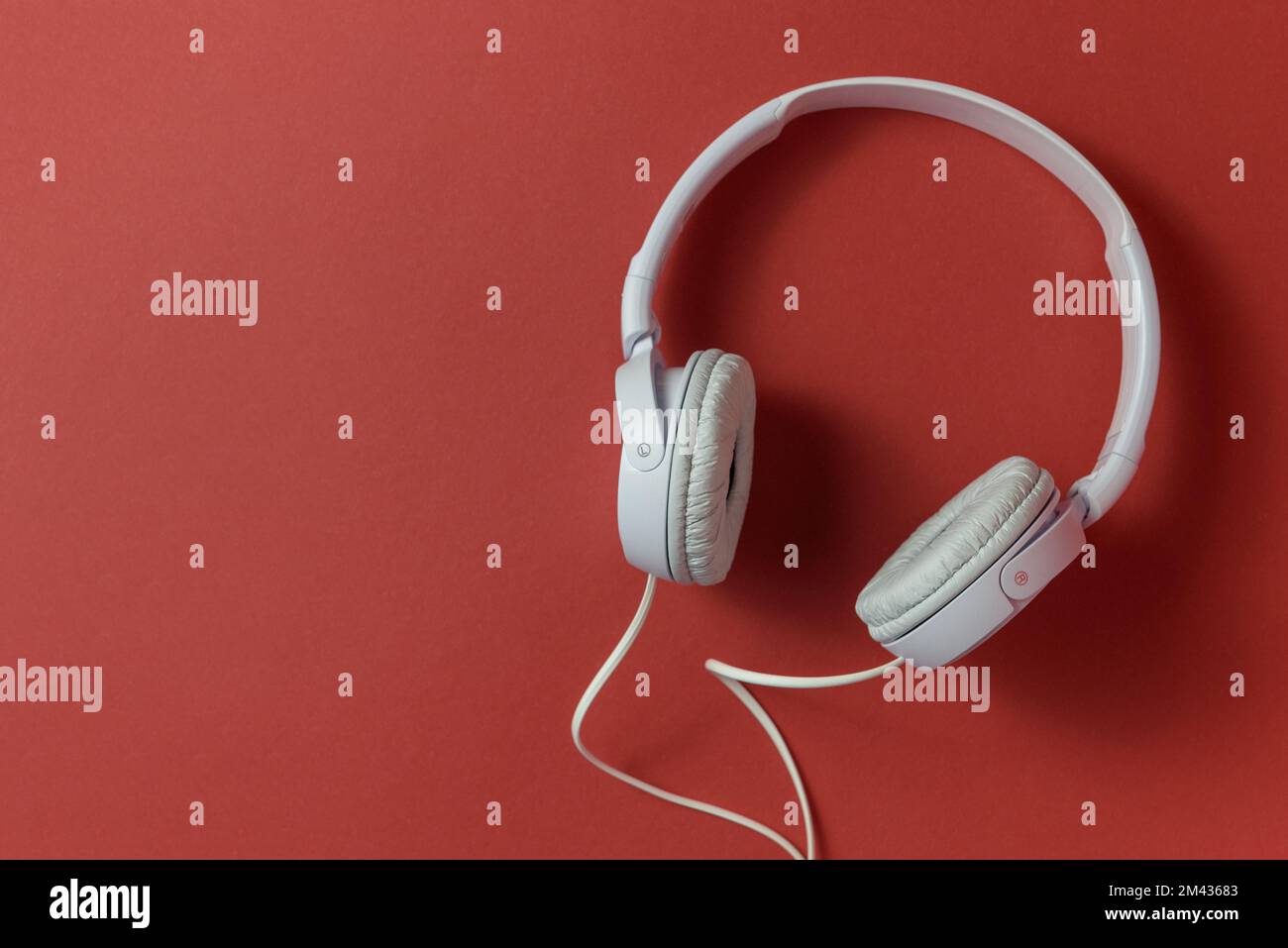 Weiße Kopfhörer mit Draht auf rotem strukturellem Hintergrund. Horizontal, Kopierbereich Stockfoto