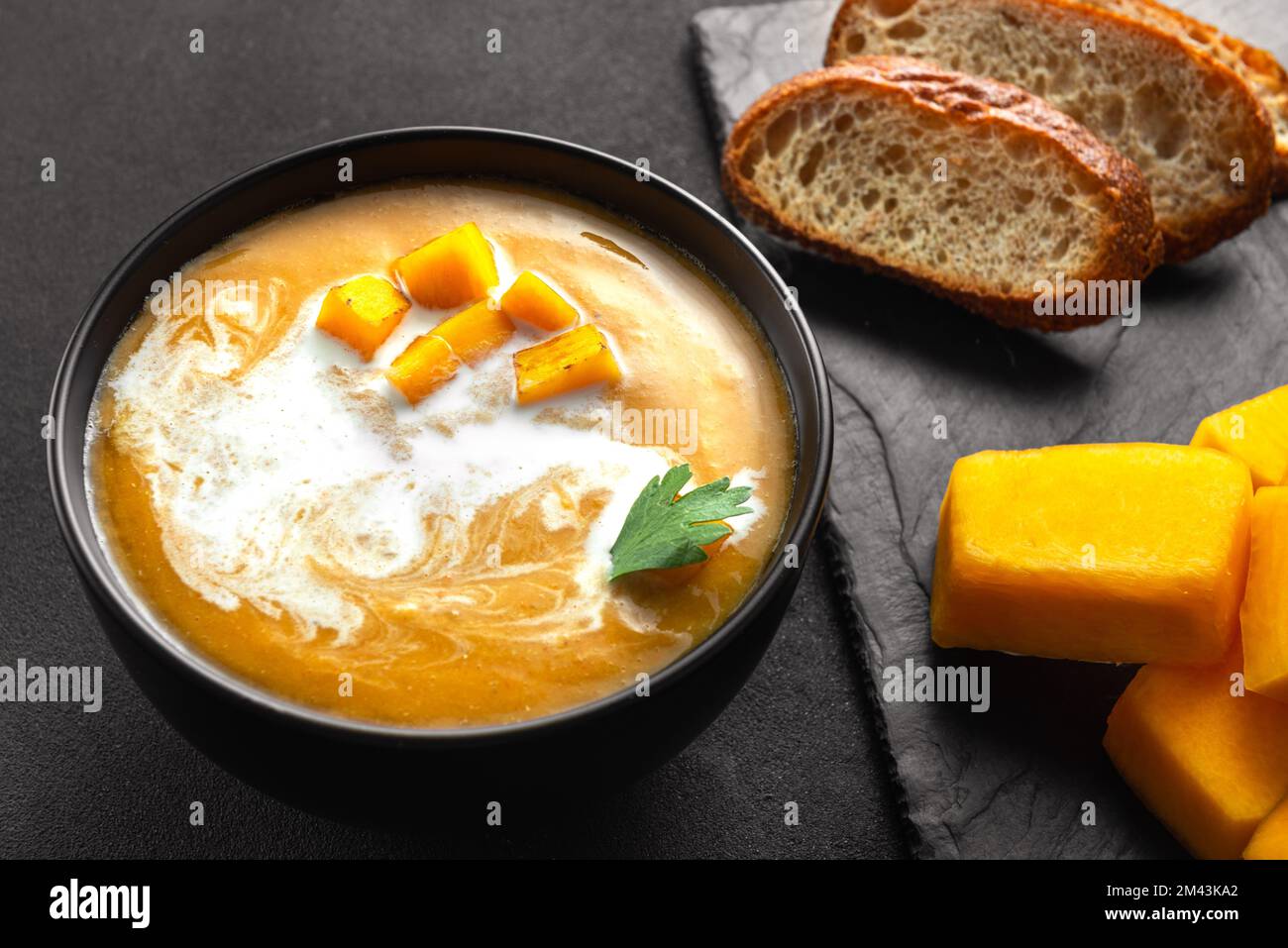 Traditionelle Kürbissuppe mit cremiger, seidiger Konsistenz. Brot und Zutaten für die Suppe nebeneinander Stockfoto