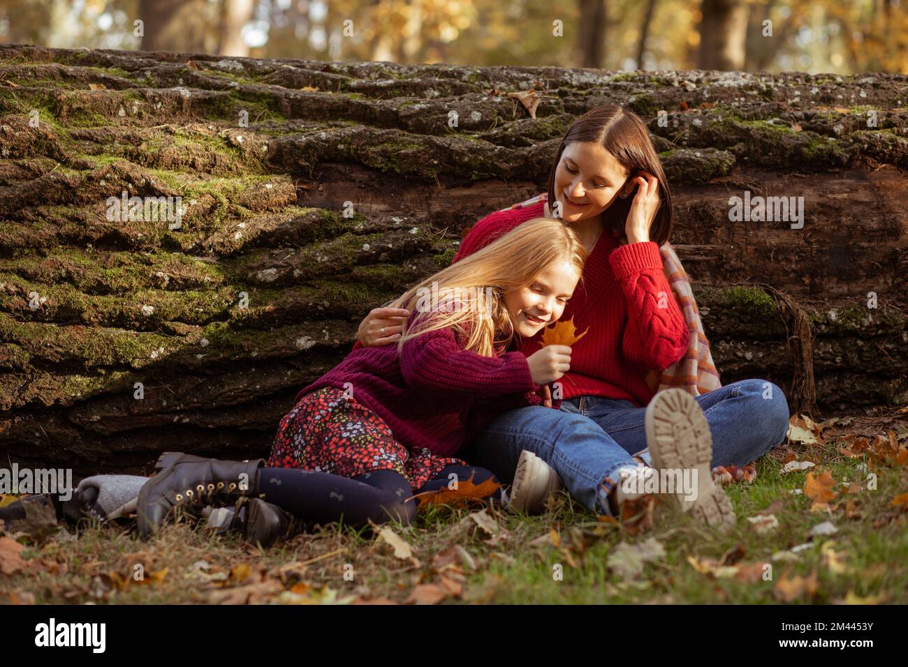 Lachende, fröhlich entspannte Mutter und Tochter, Frau und Mädchen liegen, umarmen sich beim Baumstamm mit grünem Moos während der Erkundung Stockfoto