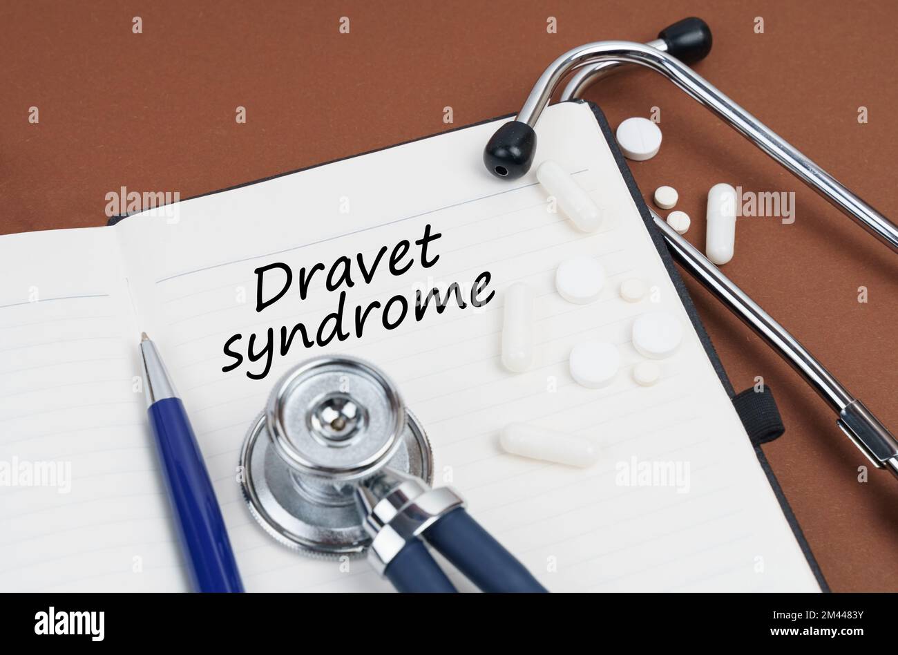 Medizin und Gesundheitskonzept. Auf einer braunen Oberfläche liegen Pillen, ein Stift, ein Stethoskop und ein Notizbuch mit der Inschrift "Dravet-Syndrom" Stockfoto