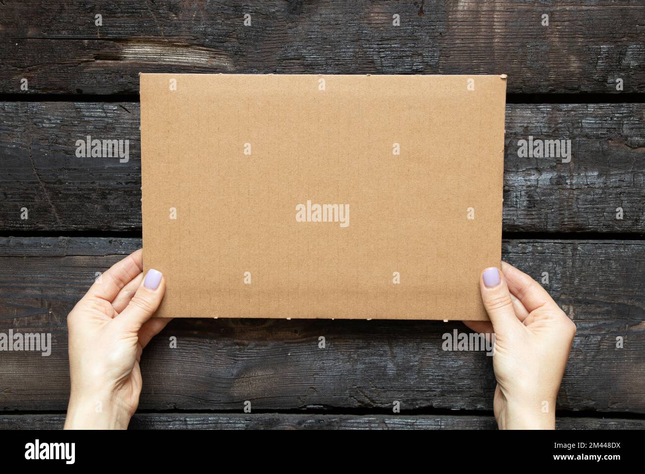 Die Hand einer Frau hält eine Pappschachtel in ihren Händen auf einem hölzernen Hintergrund, Platz für Text Stockfoto