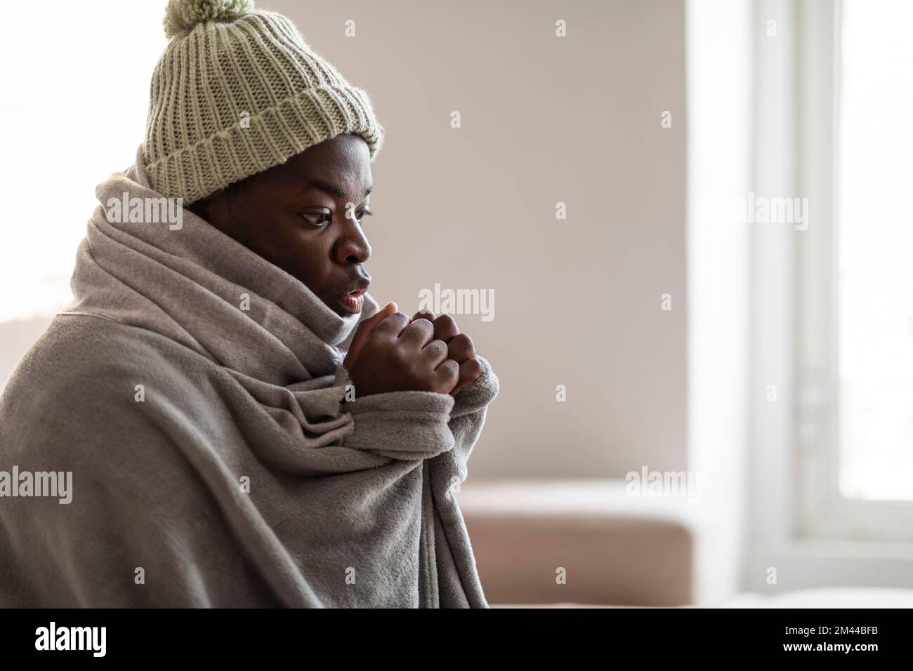 Gestresster Mann mit Hut, Decke sitzt in einem kalten Raum Stockfoto