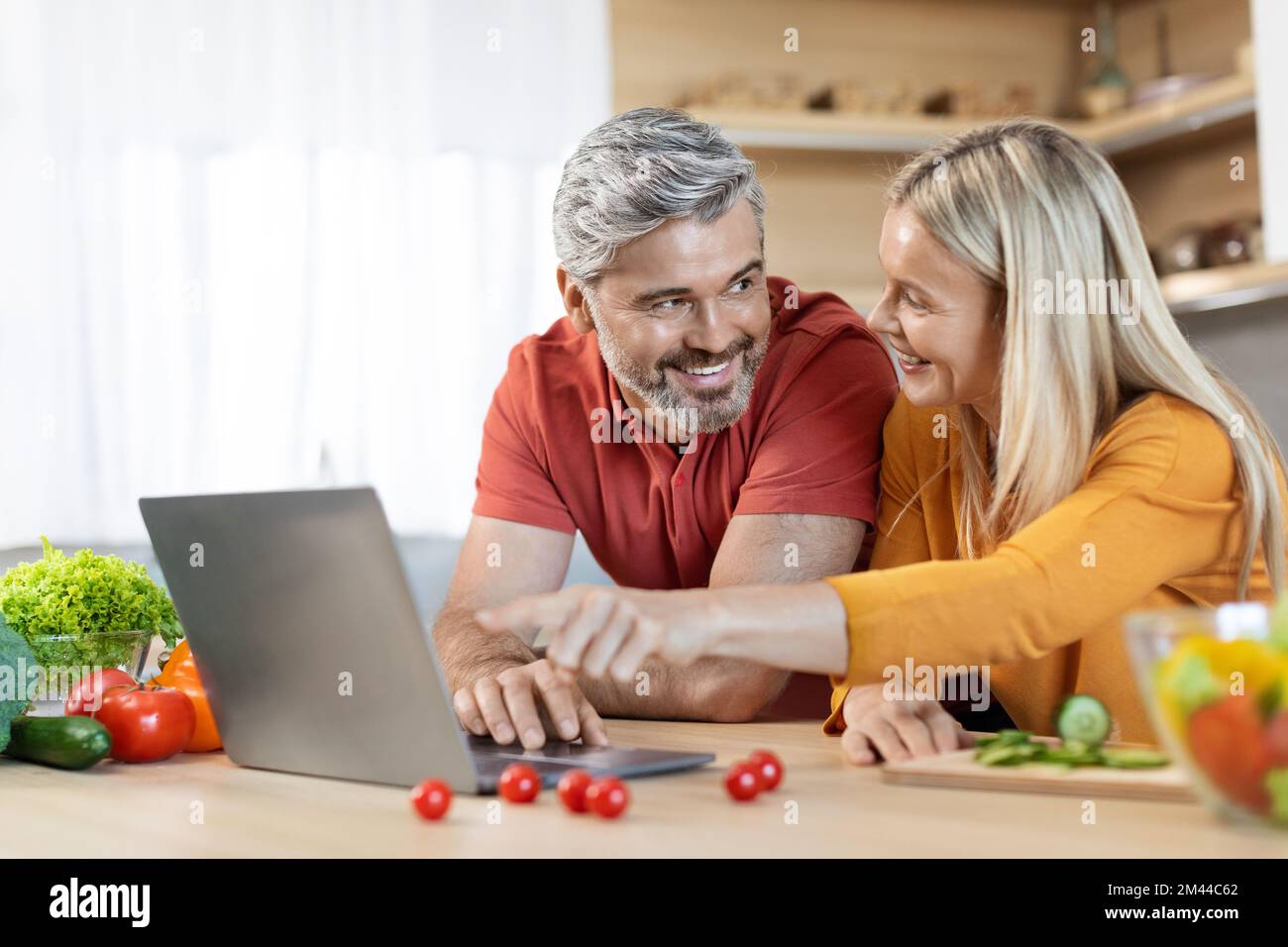 Fröhliches, reifes Paar, das im Internet nach einem guten Rezept sucht Stockfoto