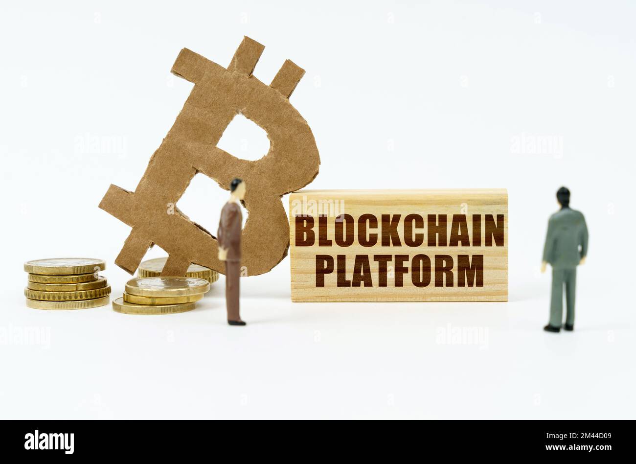 Kryptowährung und Geschäftskonzept. Auf der weißen Oberfläche der Münze befindet sich das Bitcoin-Symbol, Miniaturfiguren von Geschäftsleuten und eine Holzplatte mit der Stockfoto