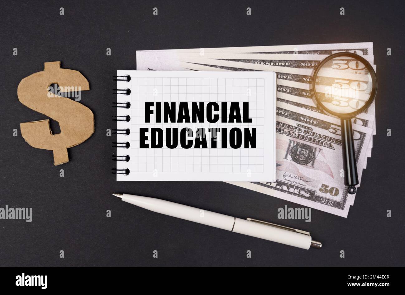 Geschäfts- und Finanzkonzept. Auf einer schwarzen Oberfläche liegen Dollar, ein Symbol, eine Lupe, ein Stift und ein Notizblock mit der Aufschrift "FINANCIAL EDUCA" Stockfoto