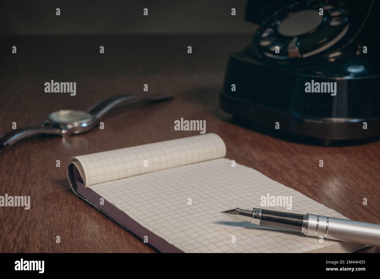Altmodische Szene. Notizblock mit leerem Blatt. Ein Tintenstift, ein altes Telefon und eine Armbanduhr. Ausgewählter Fokus Stockfoto