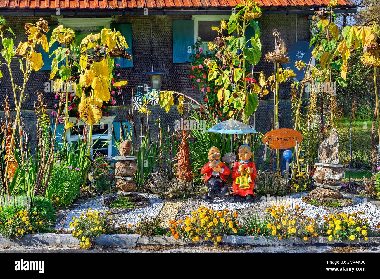 Dorfidyll, Sonnenblumen und Keramikfiguren von Oma und Opa mit Blumendekorationen, Allgaeu, Bayern, Deutschland Stockfoto