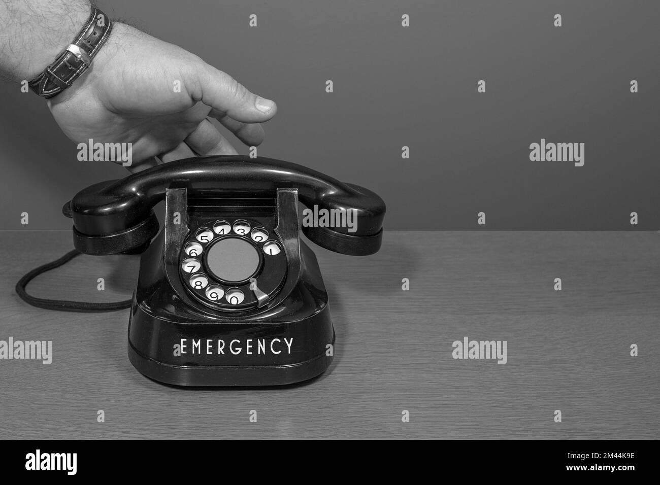 Notfall. Die Hand geht ans Telefon. Altes Telefon auf einem Holztisch, schwarz-weiß Stockfoto