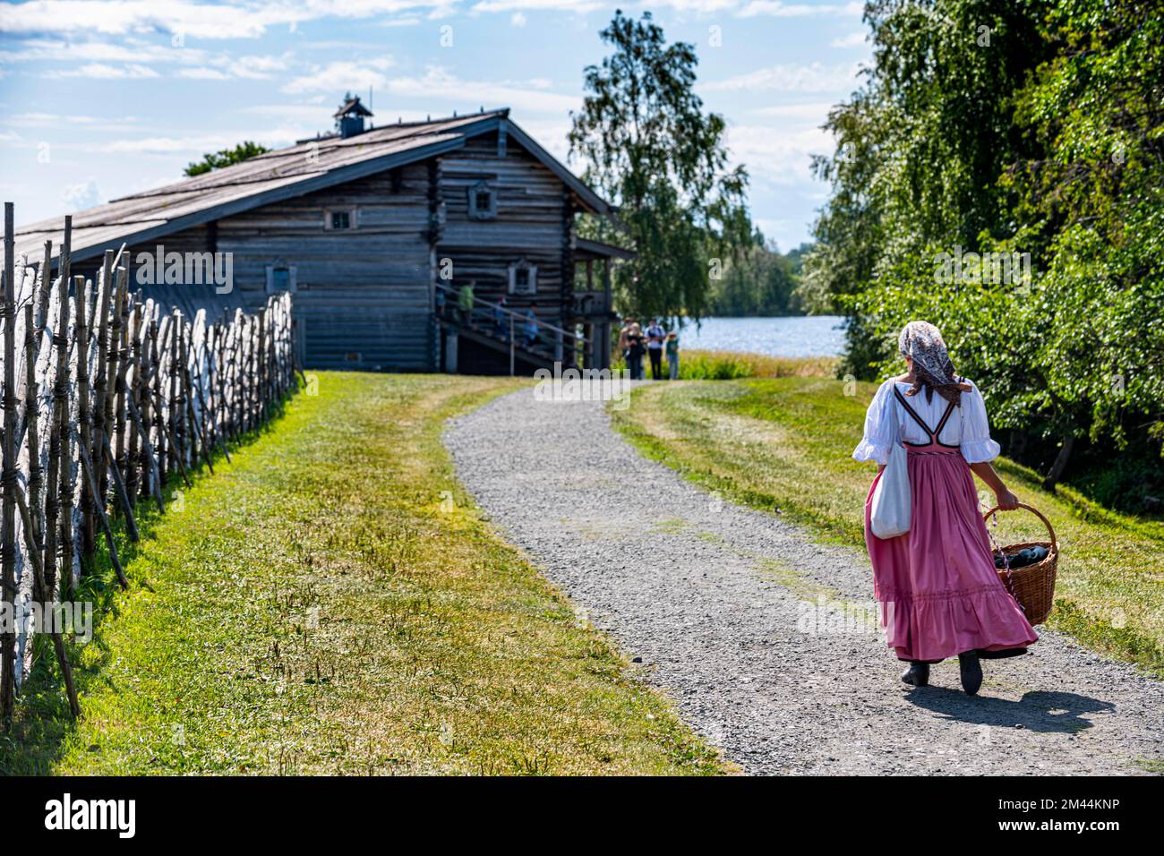 Traditionell gekleidete Frau auf dem Weg zu einem hölzernen Haus, UNESCO-Weltkulturerbe Kizhi, Karelien, Russland Stockfoto